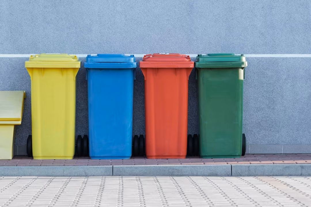 four assorted-color trash bins beside gray wall